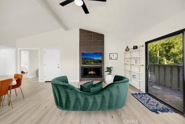 living room with vaulted ceiling with beams, light hardwood / wood-style flooring, a tile fireplace, and ceiling fan