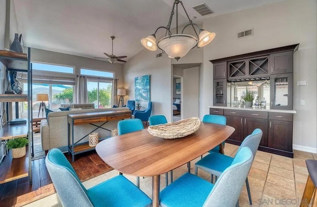 dining space featuring ceiling fan with notable chandelier, vaulted ceiling, and bar area