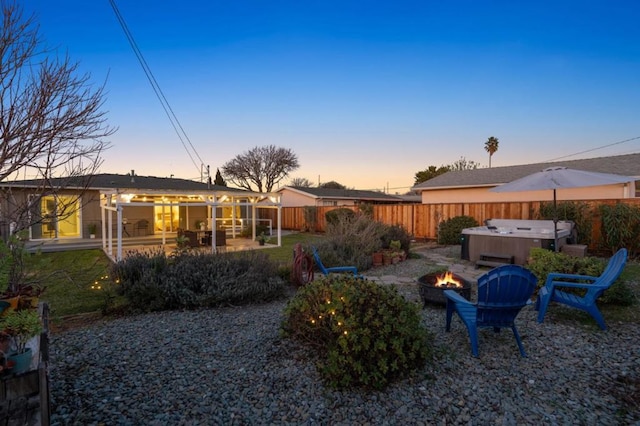 back house at dusk with a hot tub, a patio area, and an outdoor fire pit