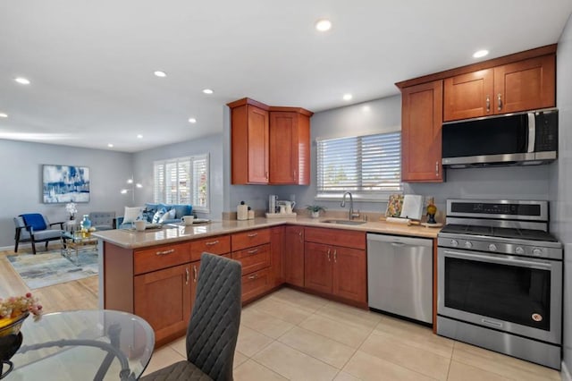 kitchen with appliances with stainless steel finishes, kitchen peninsula, sink, and light tile patterned floors