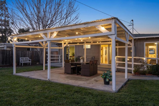 back house at dusk with a patio and a lawn