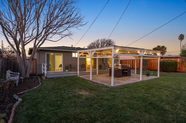 back house at dusk featuring a patio area and a lawn