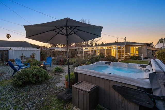 pool at dusk with a hot tub and a shed