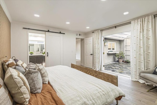 bedroom featuring ornamental molding, a barn door, ensuite bathroom, and light hardwood / wood-style floors