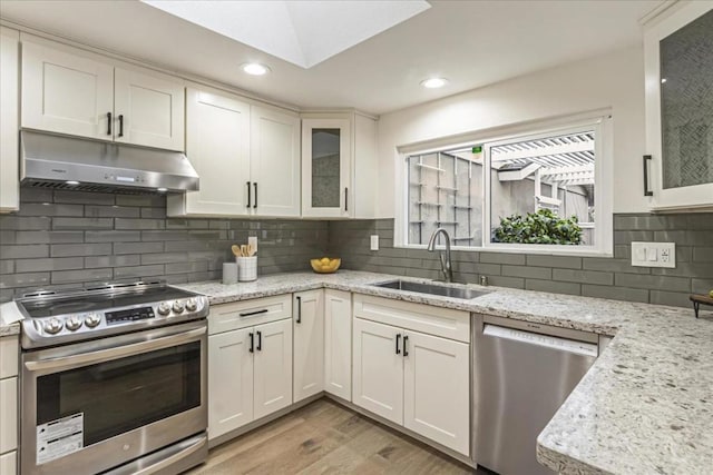 kitchen with sink, white cabinetry, appliances with stainless steel finishes, light stone countertops, and light hardwood / wood-style floors