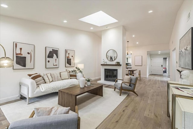 living room featuring vaulted ceiling with skylight, an inviting chandelier, and light hardwood / wood-style flooring