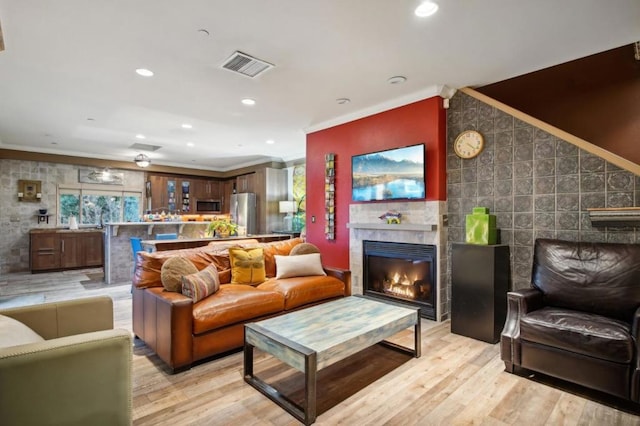 living room with crown molding, a tile fireplace, and light wood-type flooring