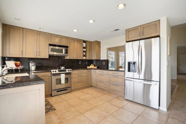 kitchen featuring sink, dark stone counters, light tile patterned floors, stainless steel appliances, and decorative backsplash