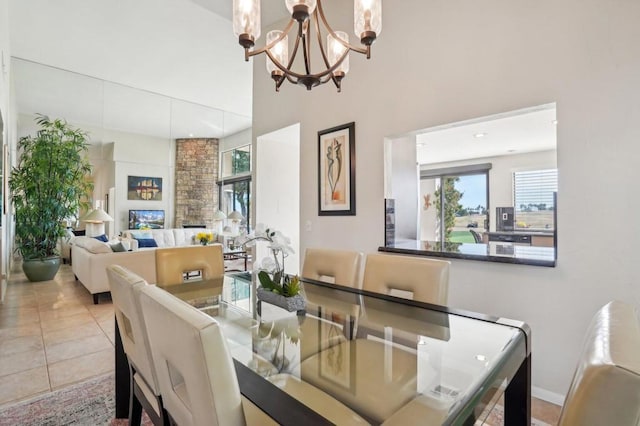 tiled dining area featuring a stone fireplace, a chandelier, and a high ceiling