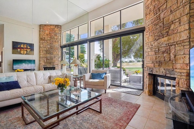 living room with a towering ceiling, a stone fireplace, and light tile patterned floors