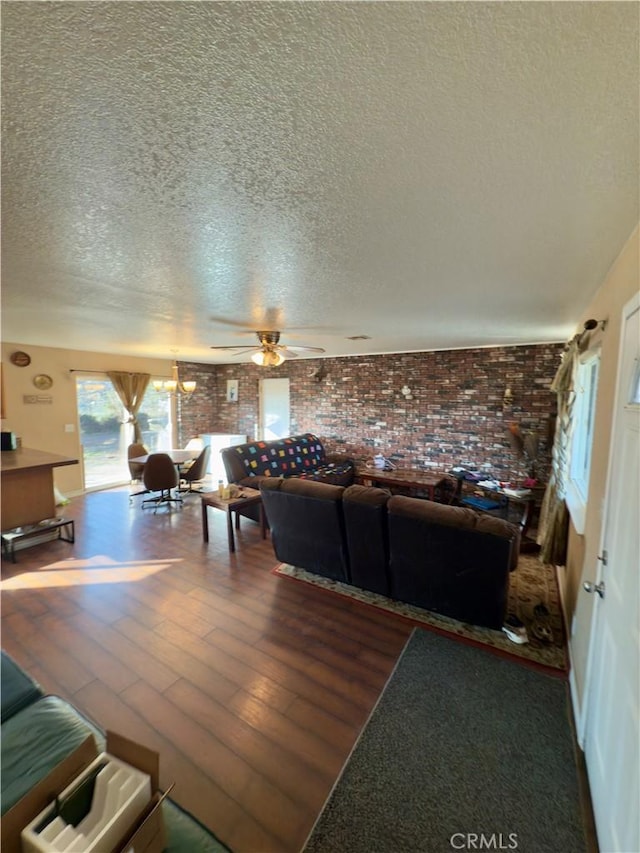 living room with ceiling fan, brick wall, dark wood-type flooring, and a textured ceiling