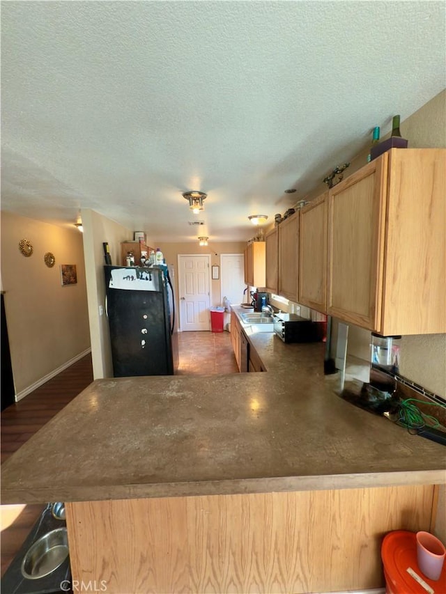 kitchen with a kitchen bar, kitchen peninsula, black fridge, light brown cabinets, and a textured ceiling