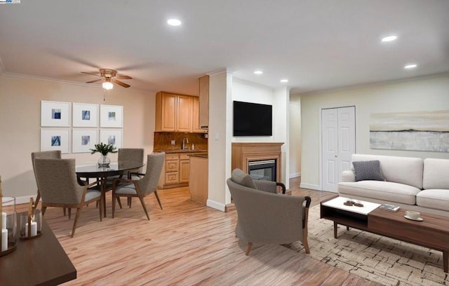 living room featuring crown molding, sink, ceiling fan, and light hardwood / wood-style floors