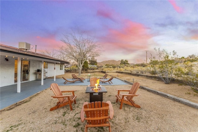 patio terrace at dusk featuring cooling unit, a mountain view, and an outdoor fire pit