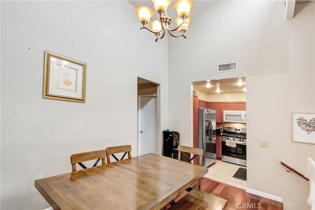 dining space featuring a towering ceiling, a chandelier, and light hardwood / wood-style floors