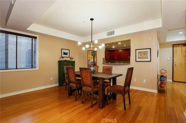 dining area featuring a raised ceiling, a notable chandelier, and light wood-type flooring