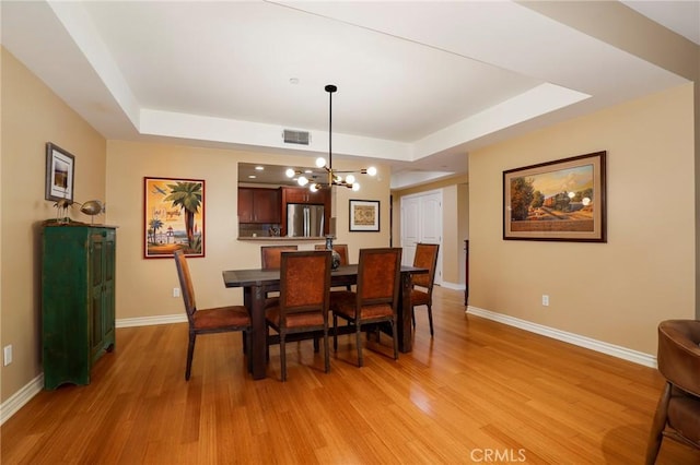 dining area with a tray ceiling, a chandelier, and light hardwood / wood-style flooring