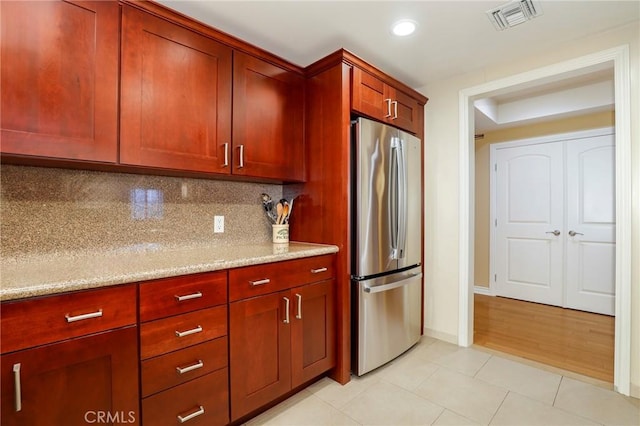 kitchen with light tile patterned flooring, light stone countertops, backsplash, and stainless steel refrigerator