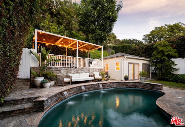 pool at dusk with an outbuilding, an outdoor hangout area, pool water feature, and a patio area