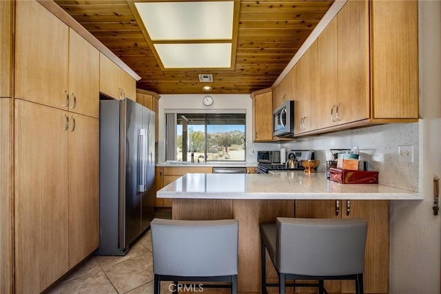 kitchen with sink, a breakfast bar, stainless steel appliances, light tile patterned flooring, and kitchen peninsula