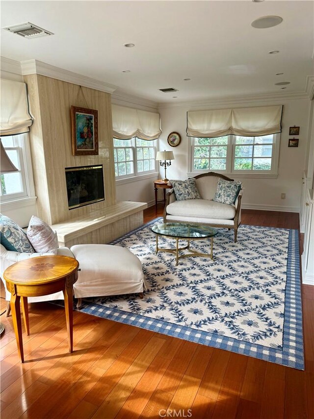 living room featuring hardwood / wood-style flooring, ornamental molding, and a large fireplace