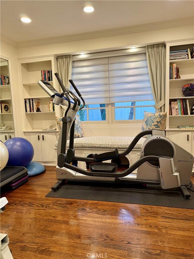 workout area with built in shelves, ornamental molding, and wood-type flooring