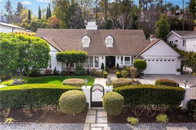 cape cod house with a gate, an attached garage, a chimney, concrete driveway, and a front lawn