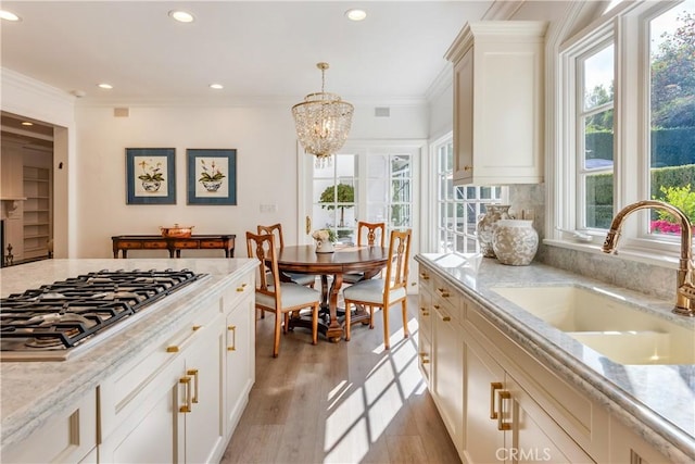 kitchen with stainless steel gas stovetop, sink, hanging light fixtures, and light stone counters