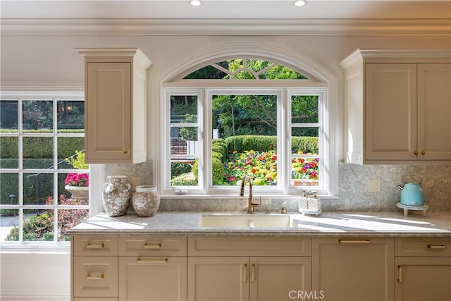 kitchen with light stone counters, recessed lighting, backsplash, and a sink