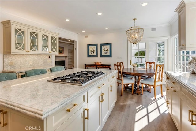 kitchen featuring light wood-type flooring, stainless steel gas stovetop, decorative light fixtures, a kitchen island, and crown molding