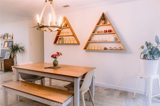 dining space with hardwood / wood-style flooring, ornamental molding, and an inviting chandelier