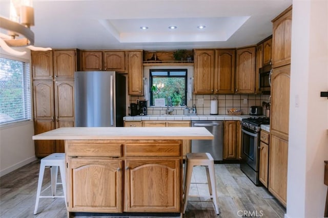 kitchen featuring a raised ceiling, a center island, appliances with stainless steel finishes, and a kitchen bar