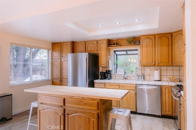 kitchen featuring stainless steel appliances, a tray ceiling, a center island, and decorative backsplash