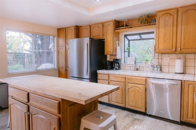 kitchen featuring sink, appliances with stainless steel finishes, tile counters, decorative backsplash, and light wood-type flooring