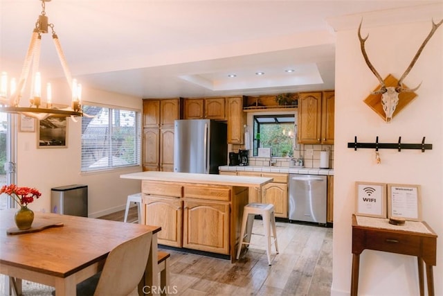 kitchen with a kitchen island, a raised ceiling, a kitchen bar, light hardwood / wood-style floors, and stainless steel appliances