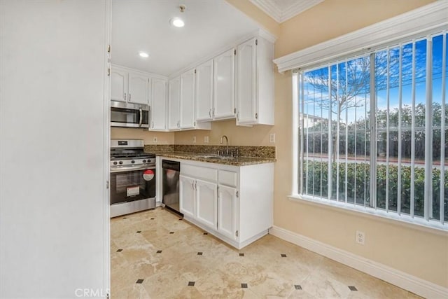 kitchen with appliances with stainless steel finishes, sink, white cabinets, dark stone counters, and ornamental molding