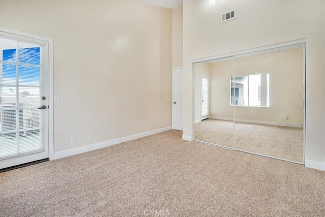 unfurnished bedroom featuring multiple windows, a closet, light carpet, and a high ceiling