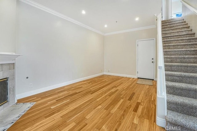 unfurnished living room with a tiled fireplace, ornamental molding, and light wood-type flooring