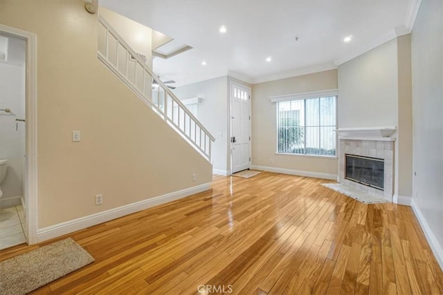 unfurnished living room with a tile fireplace, ornamental molding, and light hardwood / wood-style floors