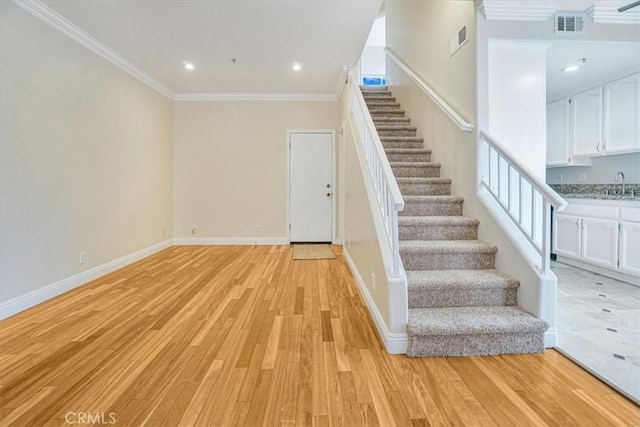 staircase featuring wood-type flooring, sink, and crown molding