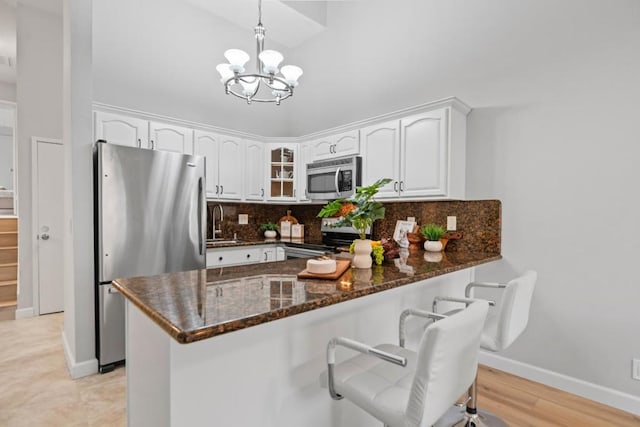 kitchen featuring tasteful backsplash, kitchen peninsula, pendant lighting, stainless steel appliances, and white cabinets