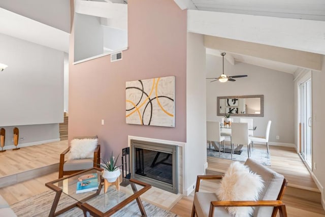 living room with ceiling fan, high vaulted ceiling, beamed ceiling, and light wood-type flooring