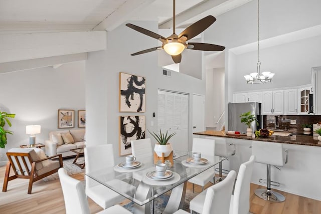 dining space with vaulted ceiling with beams, ceiling fan with notable chandelier, and light hardwood / wood-style flooring