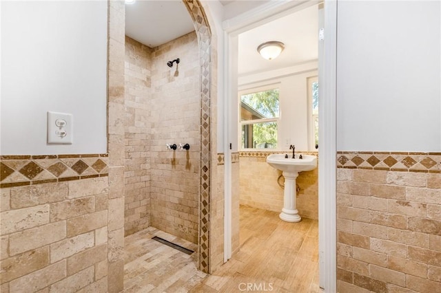 bathroom with hardwood / wood-style floors, a tile shower, and tile walls