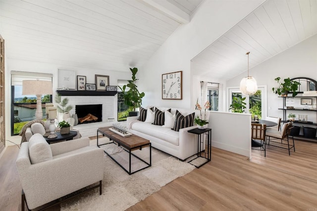 living room with beamed ceiling, a brick fireplace, a wealth of natural light, and light hardwood / wood-style flooring