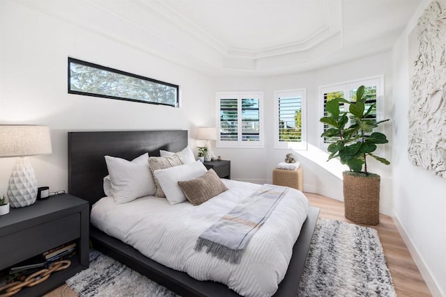 bedroom featuring crown molding, a tray ceiling, and light hardwood / wood-style flooring