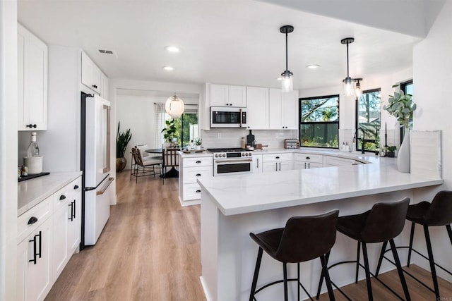 kitchen featuring hanging light fixtures, fridge, high end stainless steel range, white cabinets, and kitchen peninsula