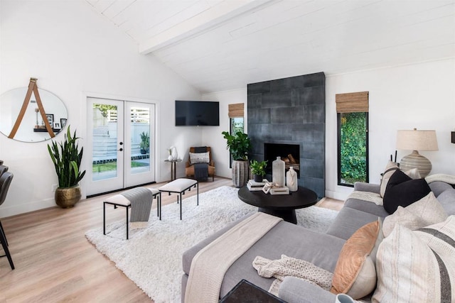 living room featuring french doors, lofted ceiling with beams, a tile fireplace, and light wood-type flooring