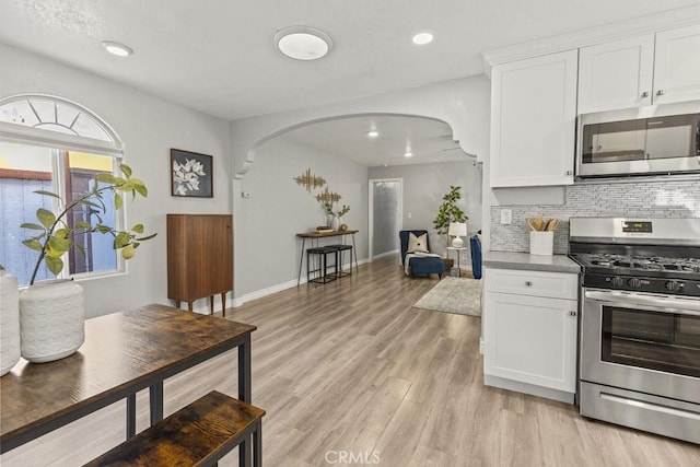 kitchen featuring backsplash, light hardwood / wood-style flooring, white cabinets, and appliances with stainless steel finishes