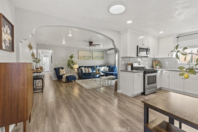 kitchen featuring tasteful backsplash, a wall mounted air conditioner, light wood-type flooring, stainless steel appliances, and white cabinets